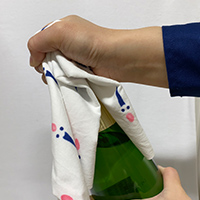 (4)ナプキンの上からコルク栓と留め金の上部をしっかりと押さえながらボトルをゆっくり回し、コルク栓を少しずつ上に持ち上げる。